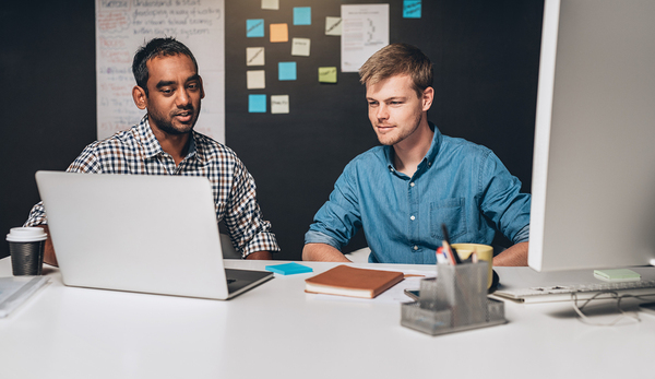 Two men working at a table looking at a laptop.